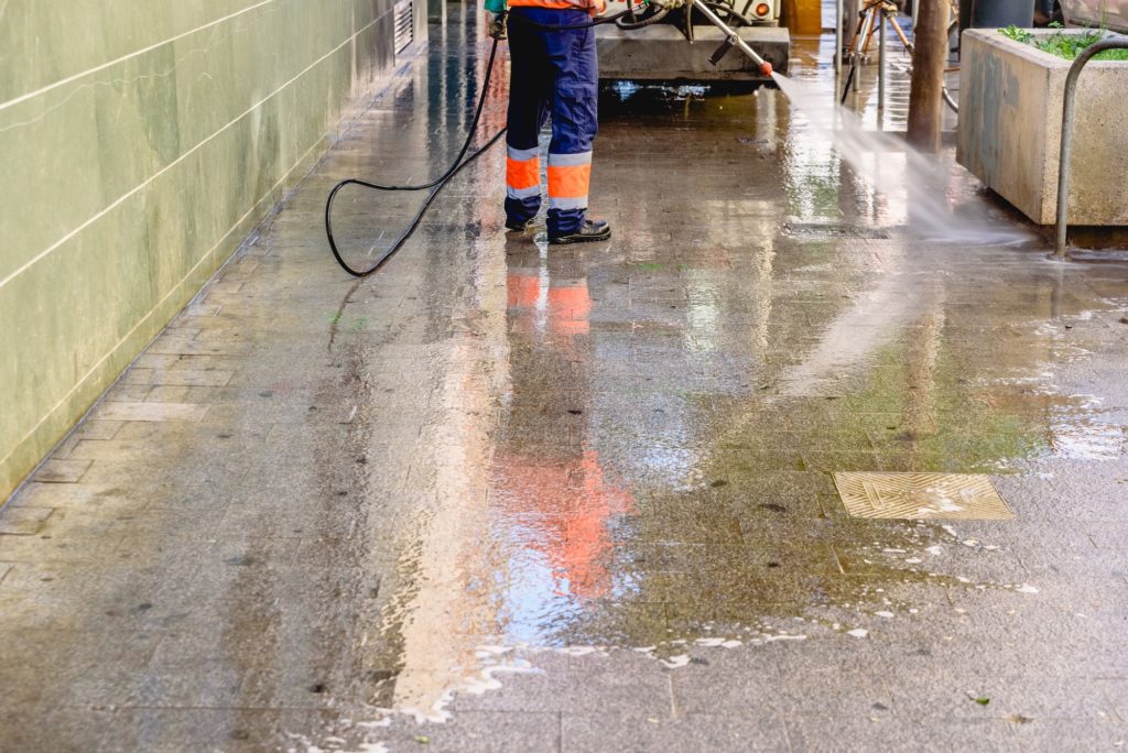 Cleaning worker throwing pressure water to clean the sidewalks of a city.